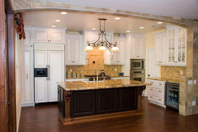 Elegant kitchen with white cabinets, dark island, granite countertops, and wood floors.