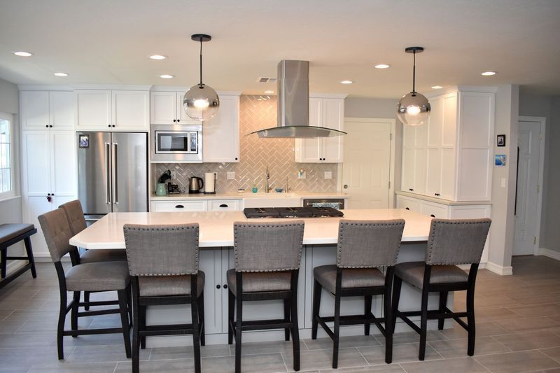 Modern white kitchen with island seating, stainless steel appliances, and pendant lights.
