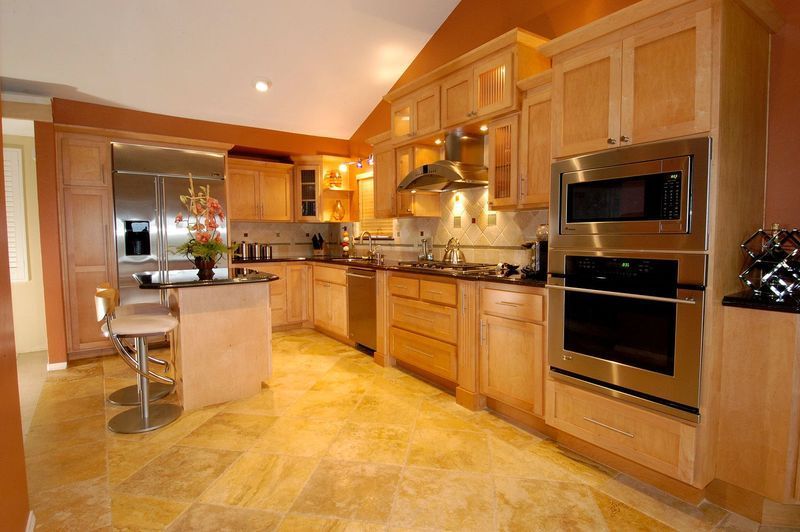 Kitchen with light wood cabinets, stainless steel appliances, and island with bar stools.