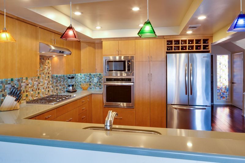 Modern kitchen with light wood cabinets, stainless steel appliances, and colorful pendant lights.