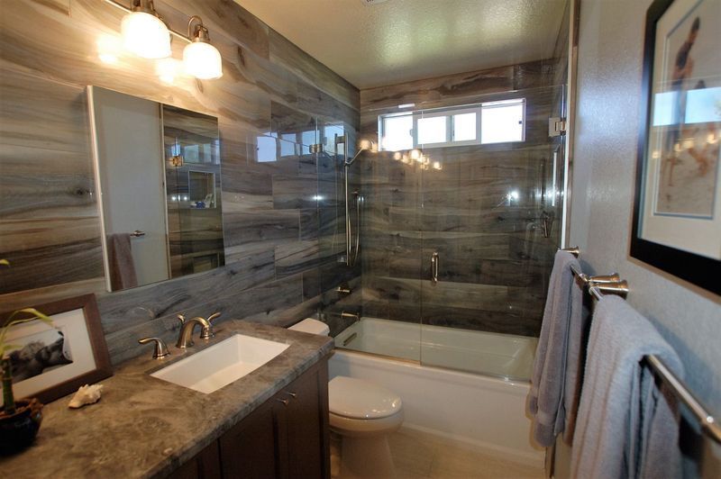 Bathroom with wooden-look tiled walls, vanity, bathtub, toilet, towels, and decorative framed picture.