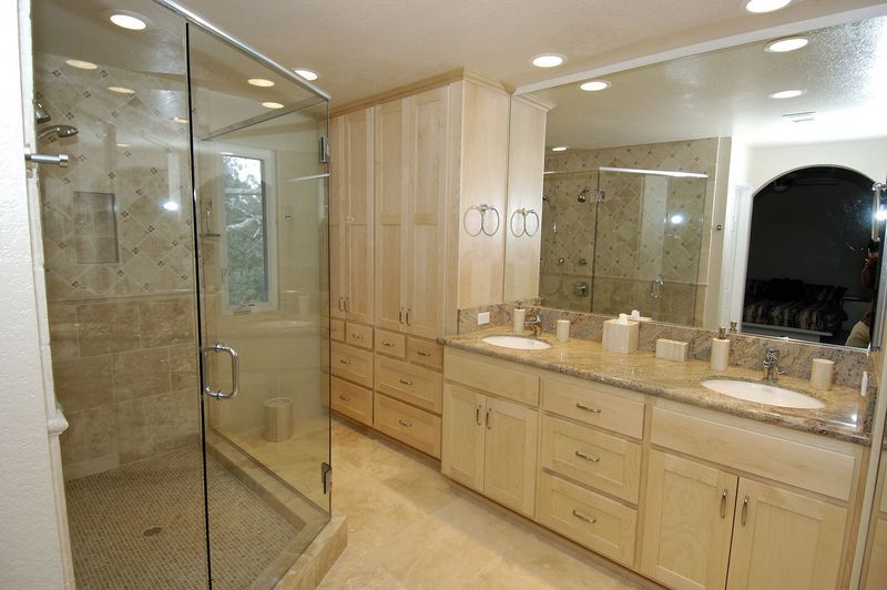 Spacious bathroom with glass shower, double sinks, light wood cabinets, and large mirror.