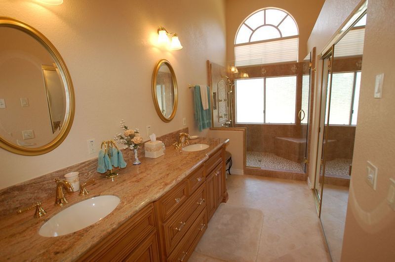 Bathroom with double vanity, golden framed mirrors, and a glass-enclosed shower.