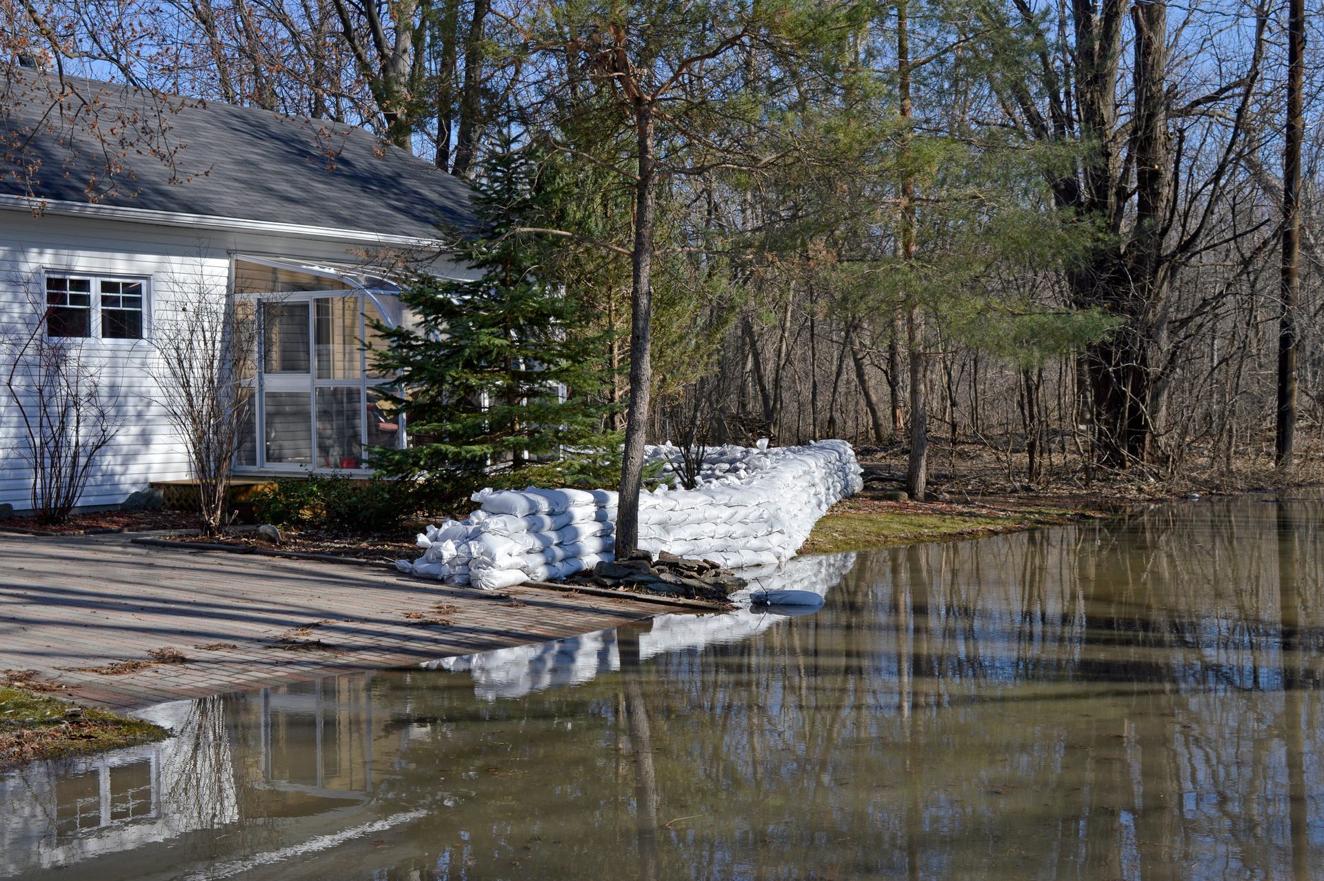 White house beside flooded yard with snowbanks and trees reflected in standing water