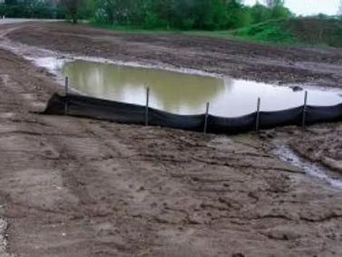 Mud-filled construction pond with black silt fence around the edge.