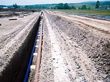 Long dirt road under construction with a narrow drainage trench running down the center under a clear sky