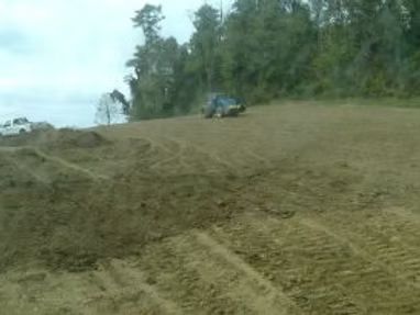 Plowed field with a tractor near a tree line under a cloudy sky