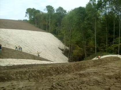 Workers on a sloped dirt embankment beside a forested hillside construction site