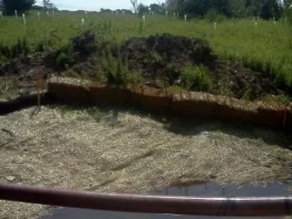 Empty concrete pit with debris and a rusted pipe in front of a grassy field