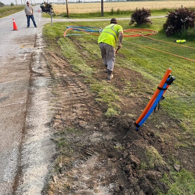 Roadside utility workers marking underground lines near a muddy roadside ditch