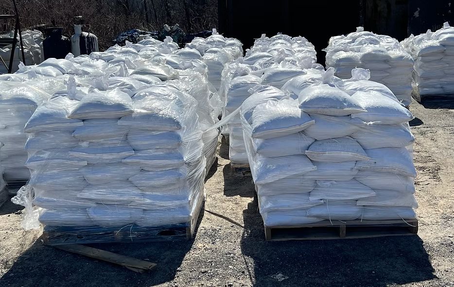 Pallets stacked with white bags outdoors in a snowy yard, with more piles in the background.