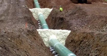 Green pipeline laid in a muddy trench, with white insulation and a worker in the background.