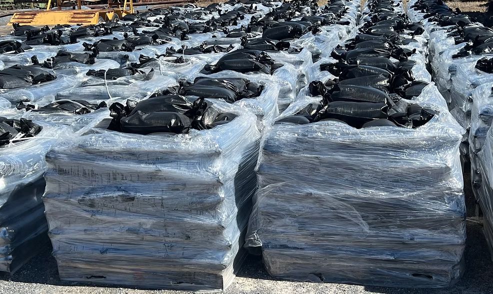 Pallets of black tires wrapped in plastic stacked in an outdoor industrial yard under snow