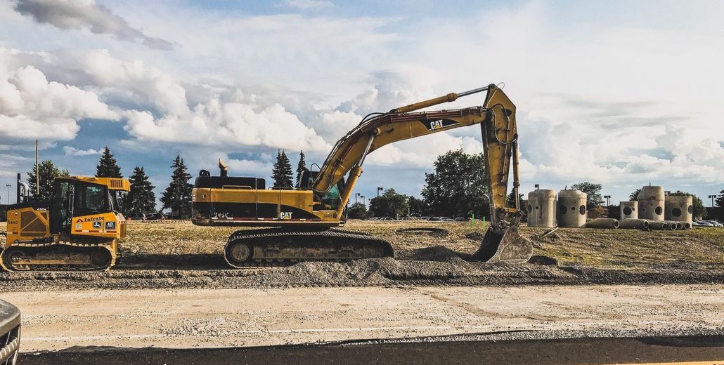 Yellow excavator and bulldozer on construction site, cloudy sky in background.