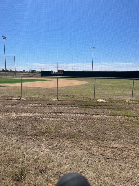 a baseball field with a fence and a helmet in the foreground
