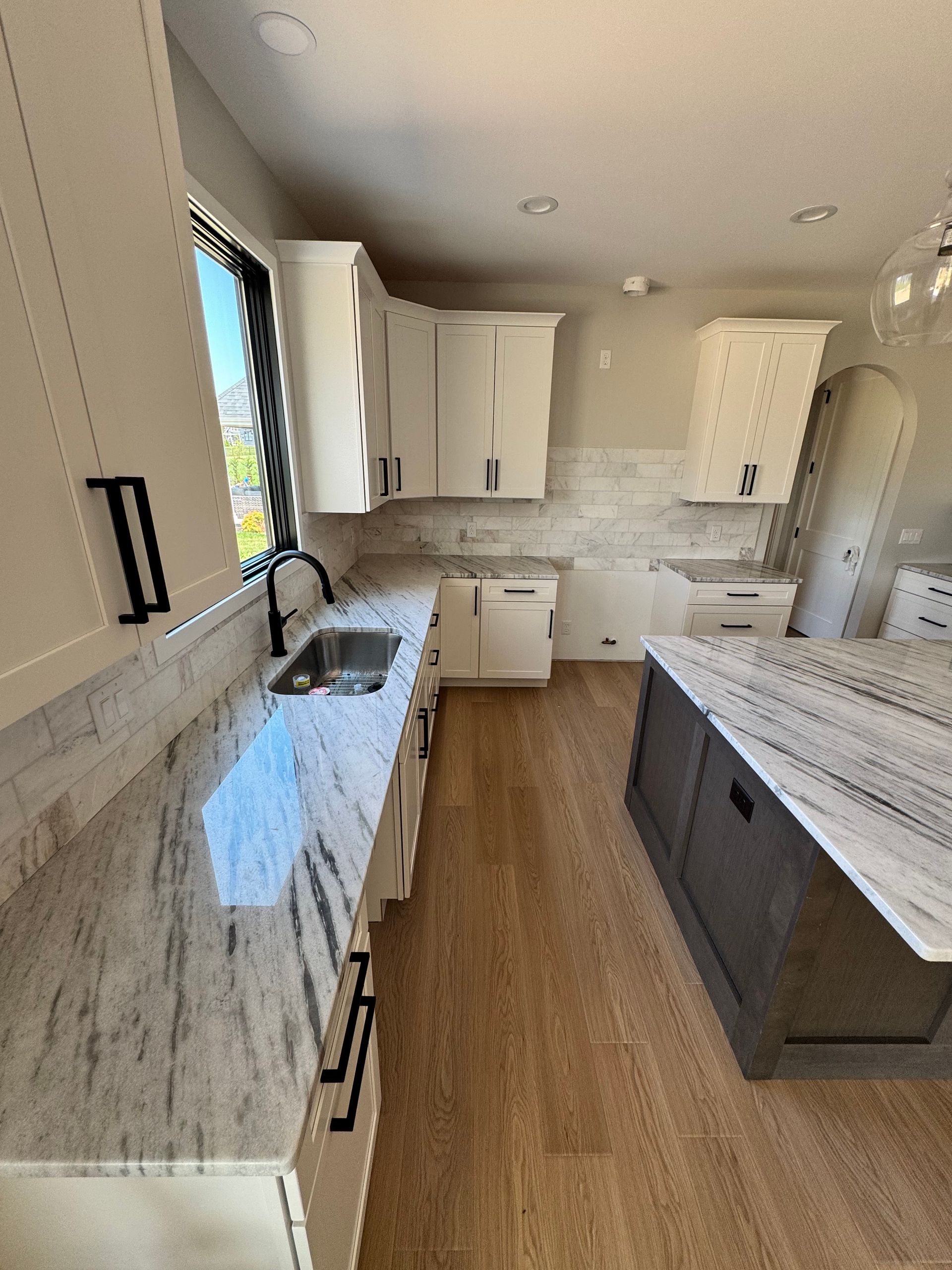 A kitchen with white cabinets , granite counter tops , a sink , and a large island.