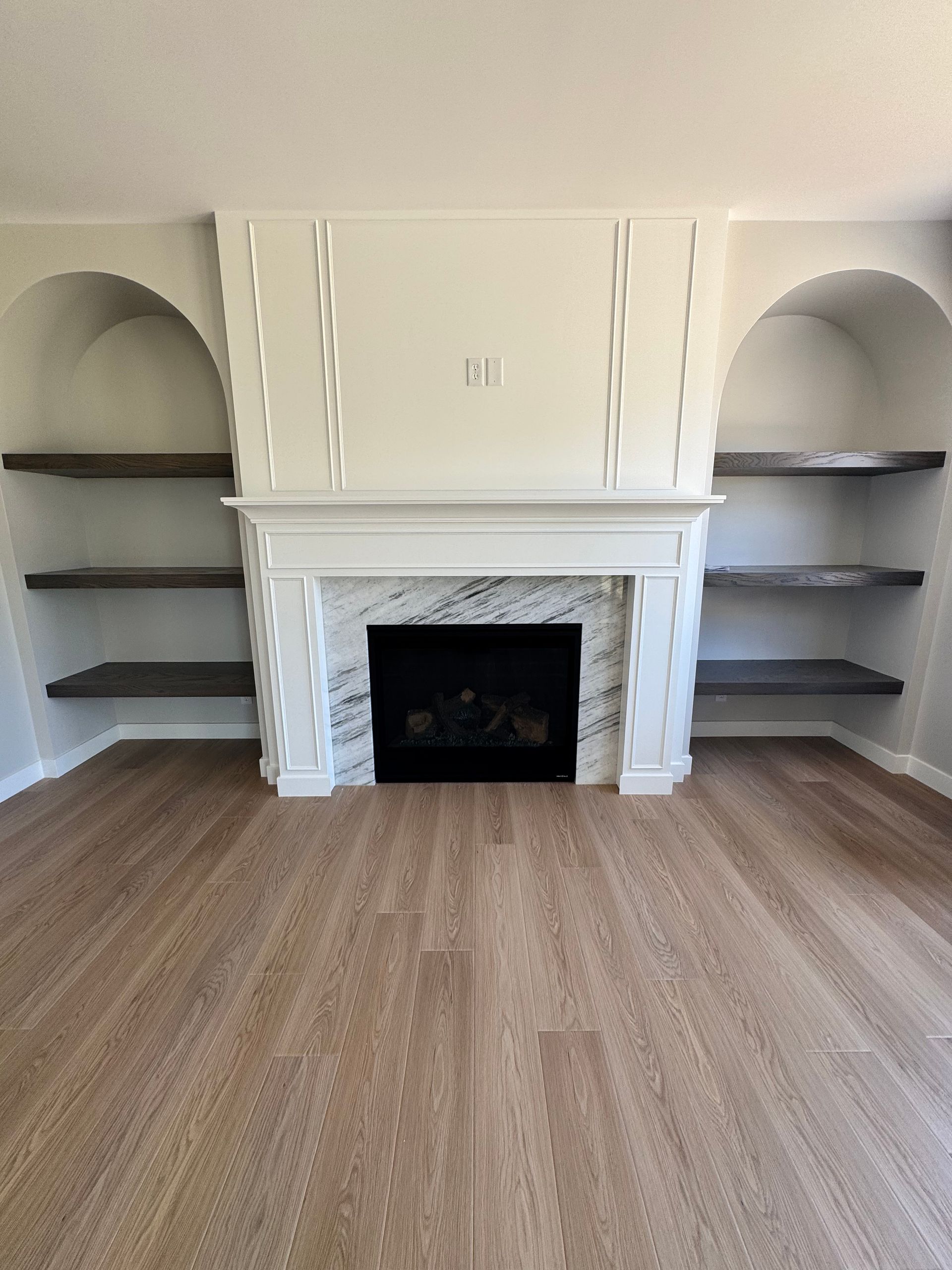 An empty living room with a fireplace and shelves.