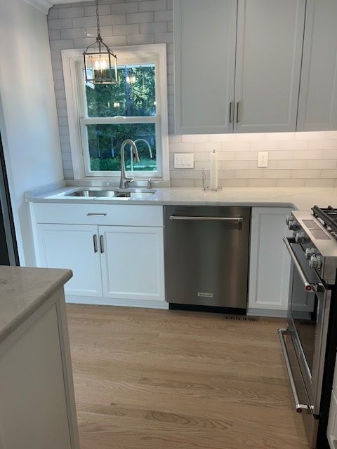 A kitchen with white cabinets , stainless steel appliances , a sink and a window.