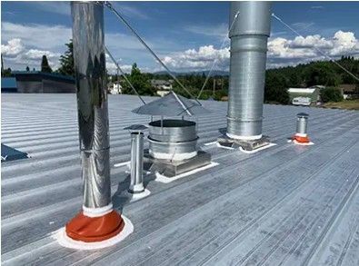 Metal rooftop with vents, chimney pipes, and flashing under a blue sky.