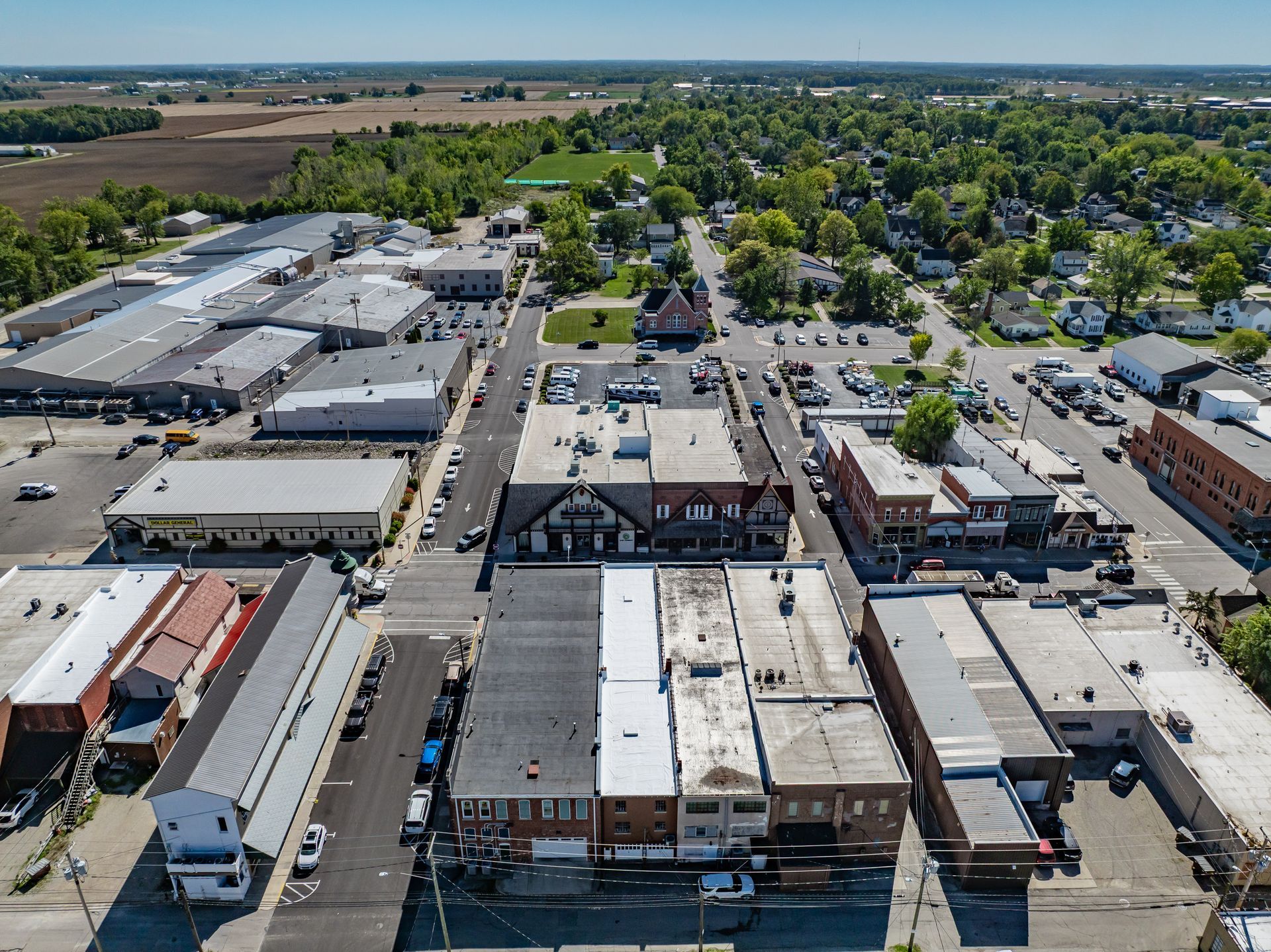 Aerial view of a small town main street with low buildings, parked cars, and surrounding farmland
