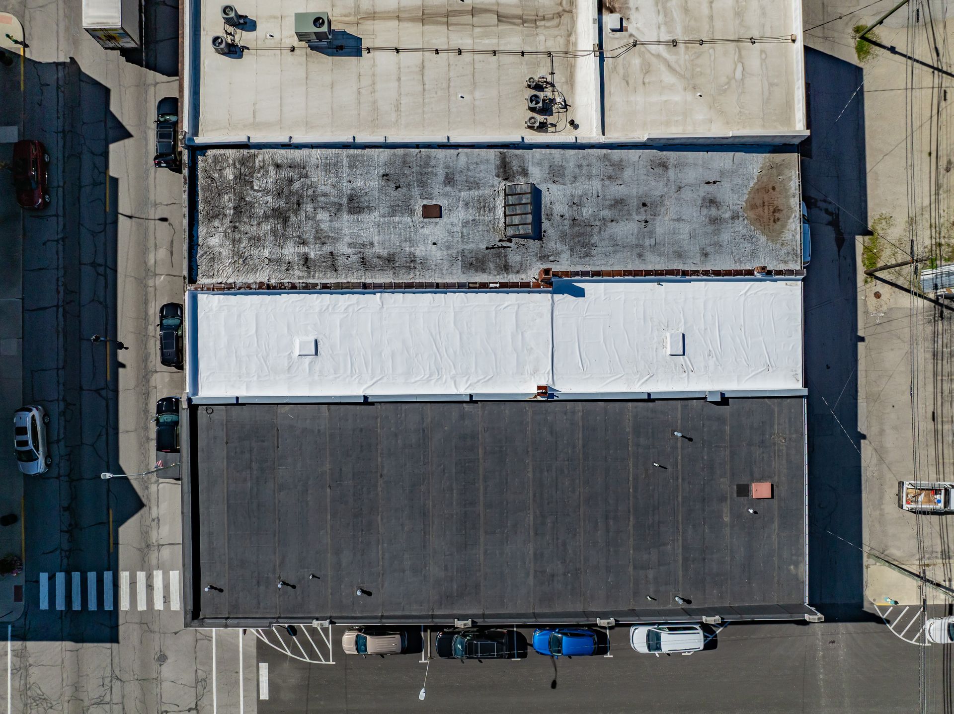 Aerial view of three connected flat-roof buildings with parked cars along a street.