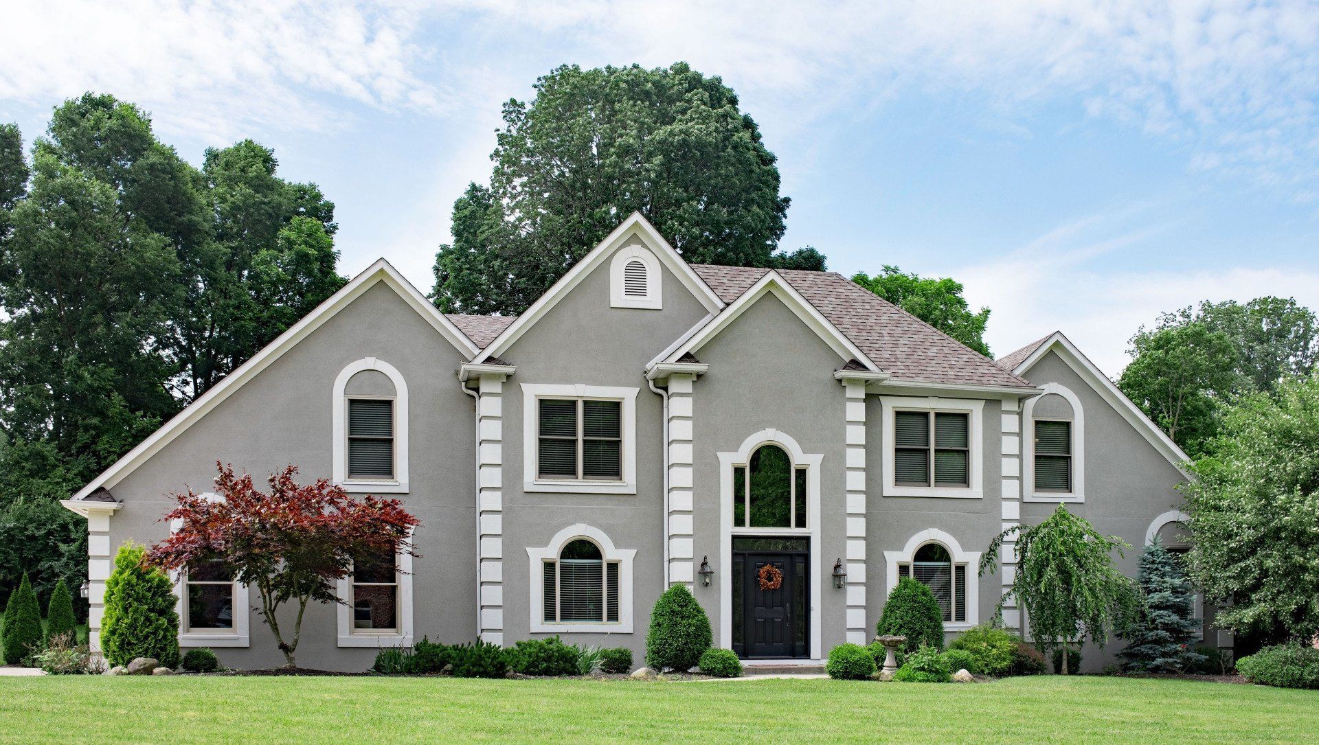 Gray suburban house with white trim, front lawn, and trees under a blue sky