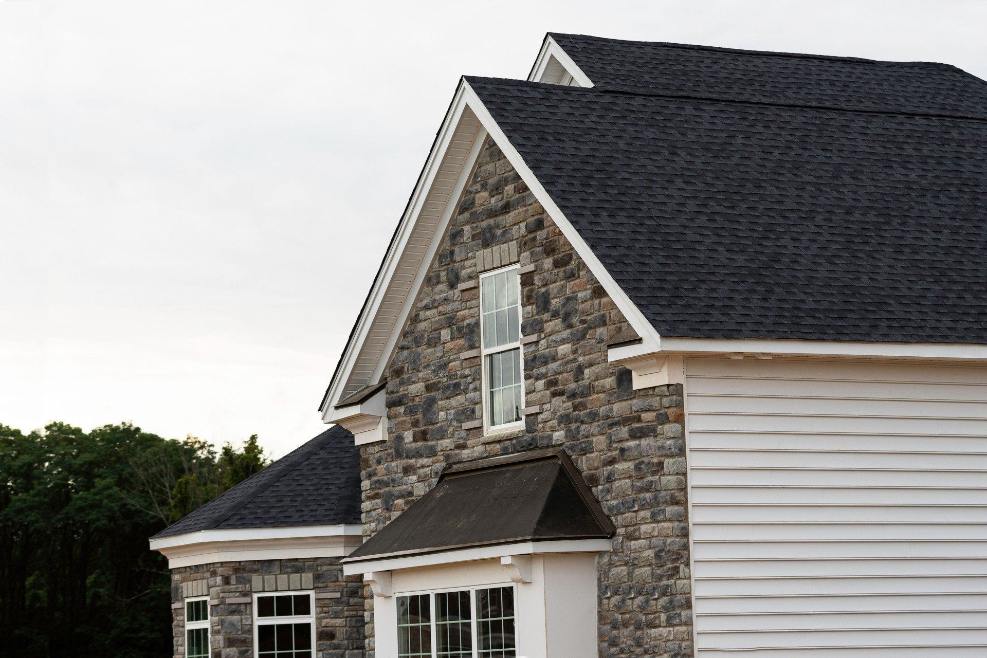 Suburban house with stone siding, white trim, and dark shingled roof