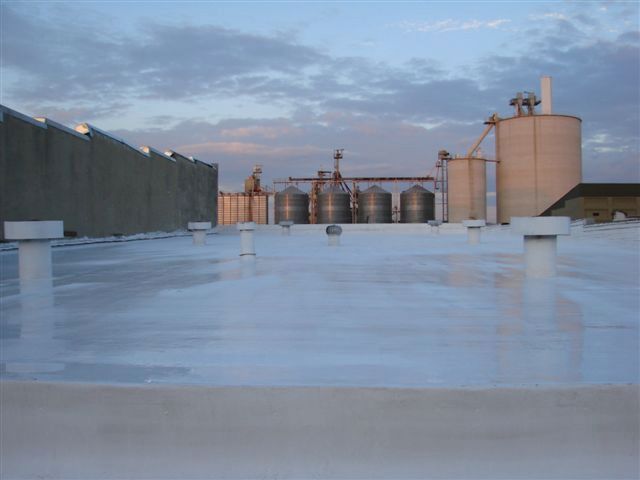 Industrial rooftop with large tanks and a white reflective surface at sunset