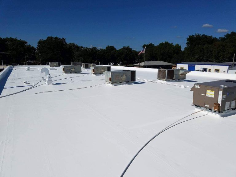 White flat rooftop with HVAC units and vents under a clear blue sky