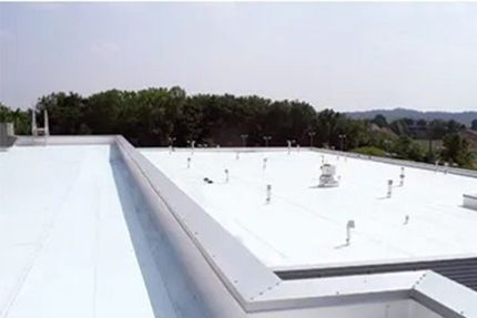 White flat rooftop with HVAC vents and trees in the background