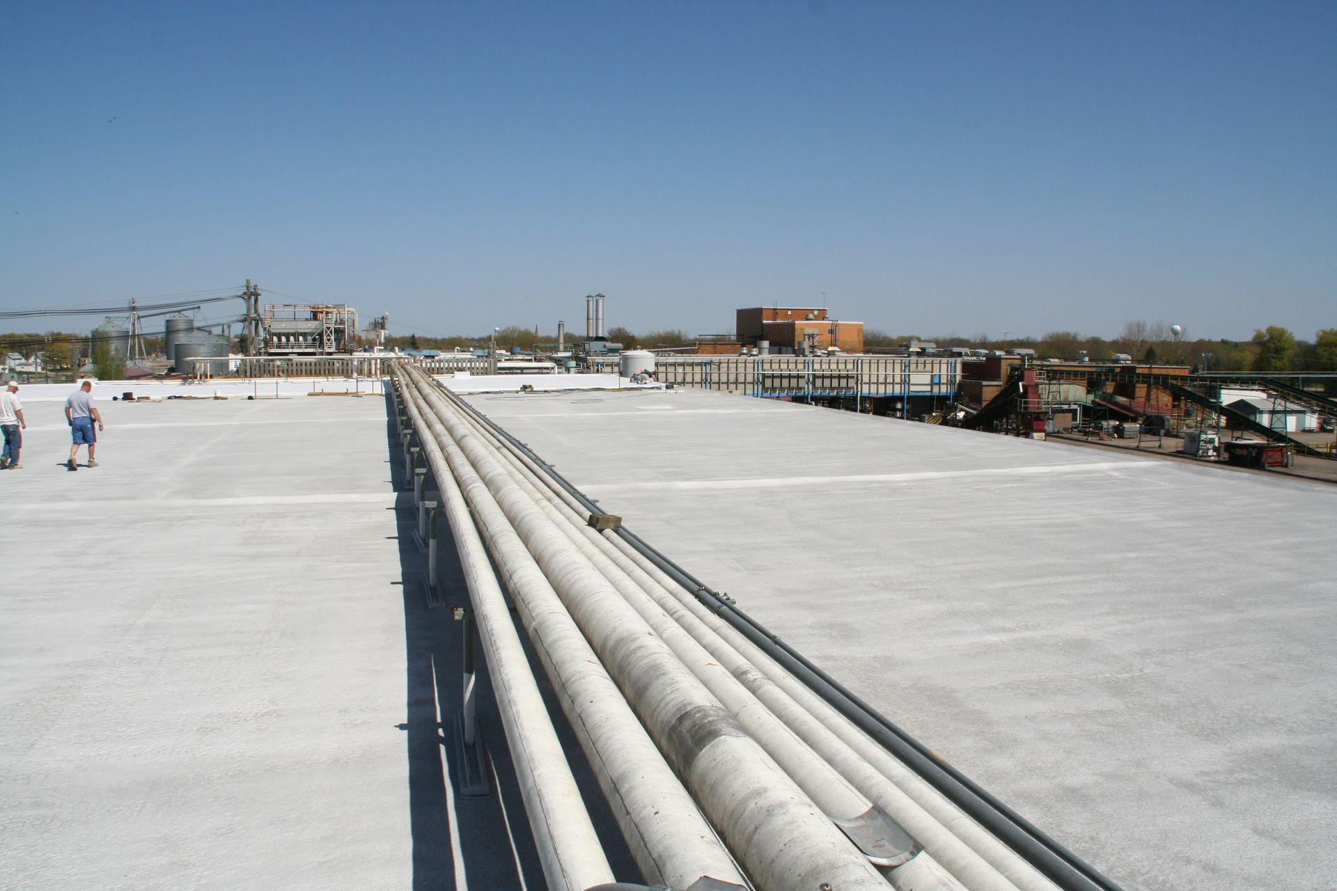 Rooftop with white waterproofing and long gray pipes stretching into the distance under a clear blue sky