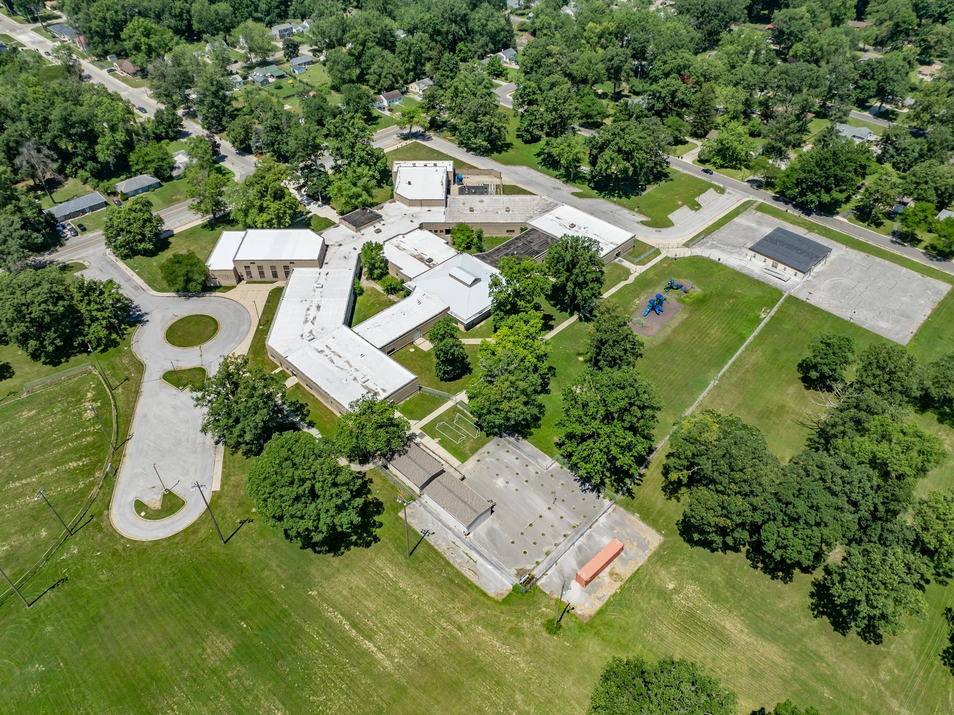 Aerial view of a white-roofed building complex surrounded by trees and grassy fields