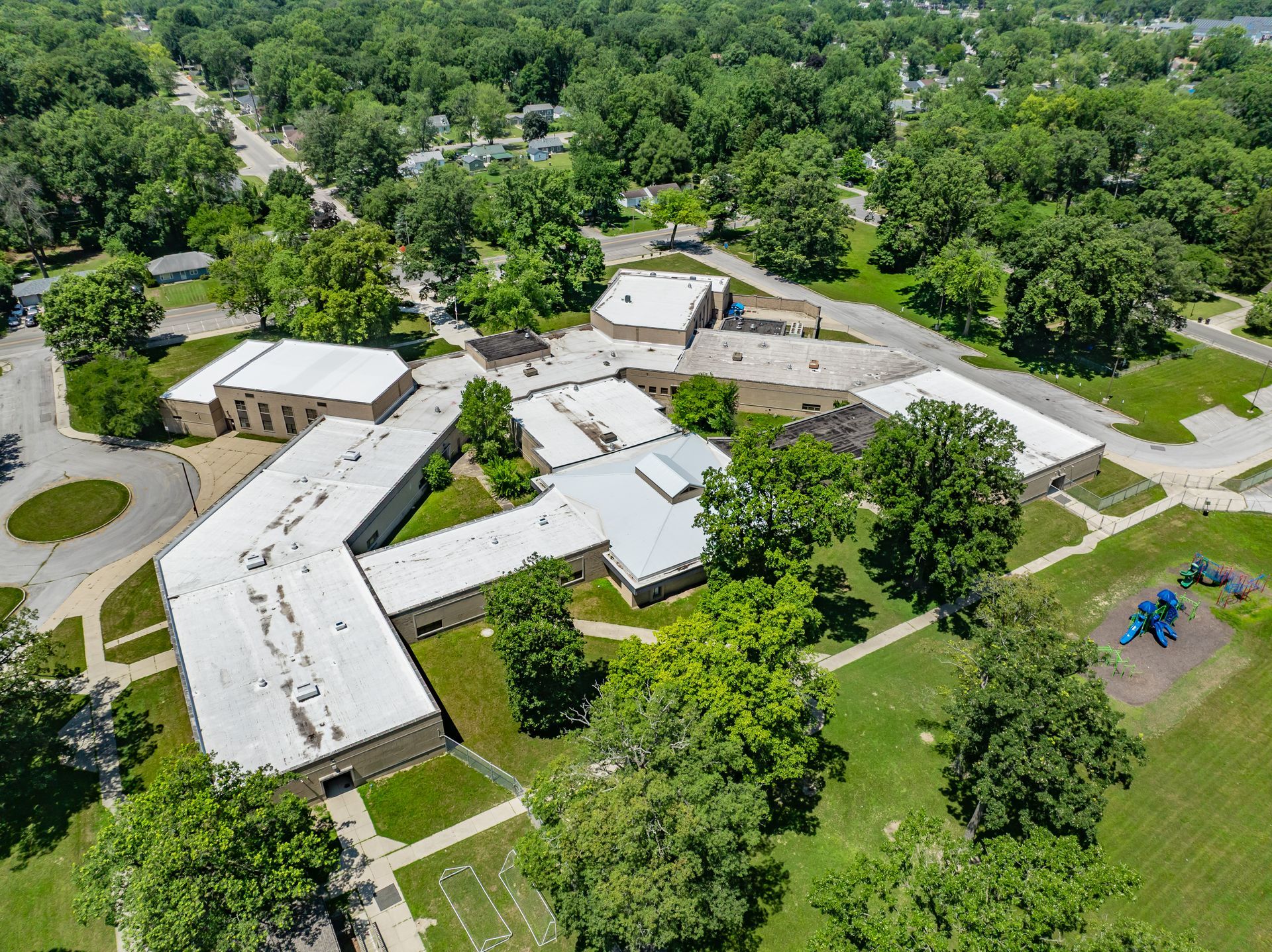 Aerial view of a U-shaped white building complex surrounded by trees and grassy grounds.