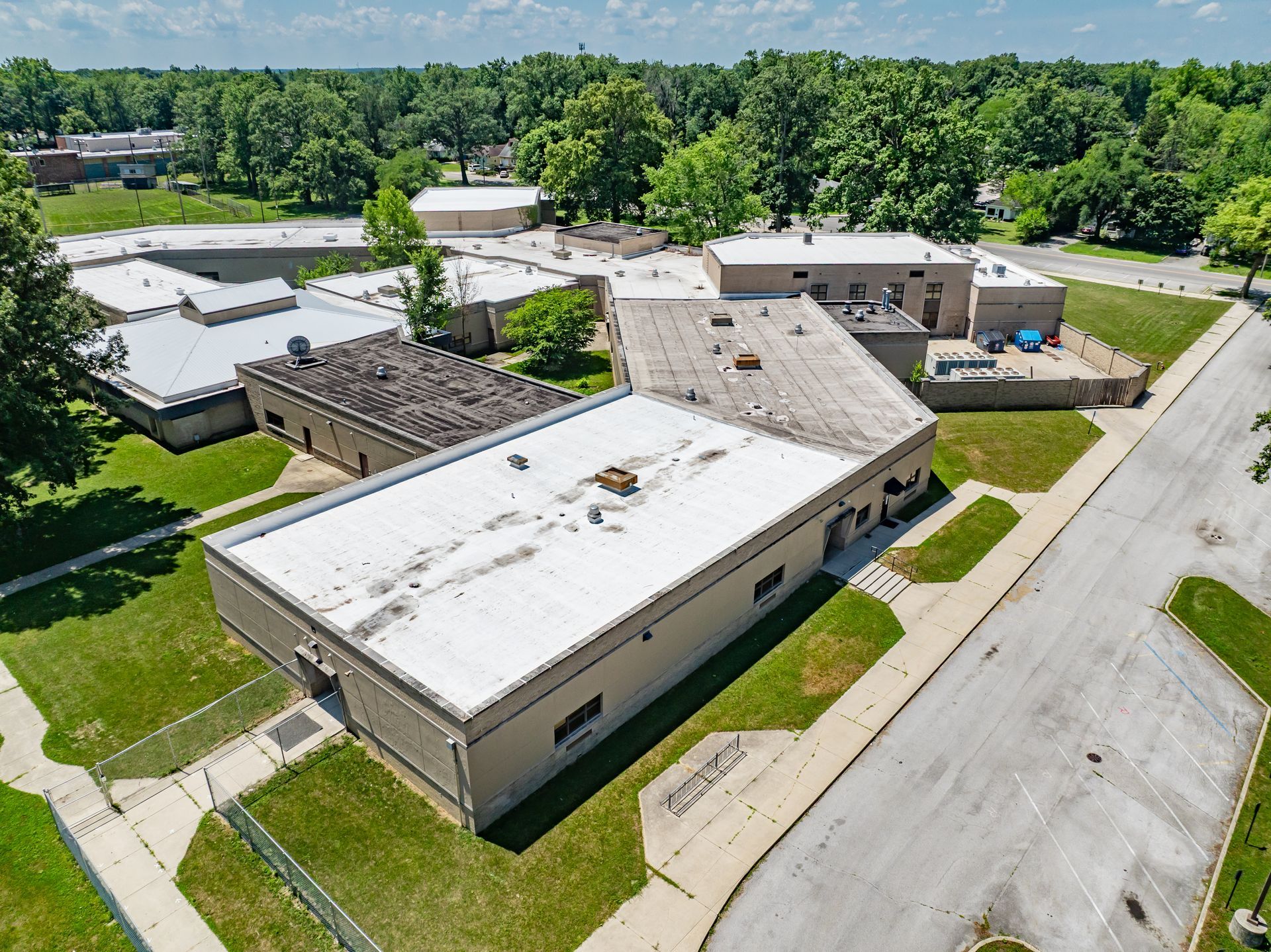 Aerial view of a low-rise office complex with white roofs and parking lot beside a tree-lined road.