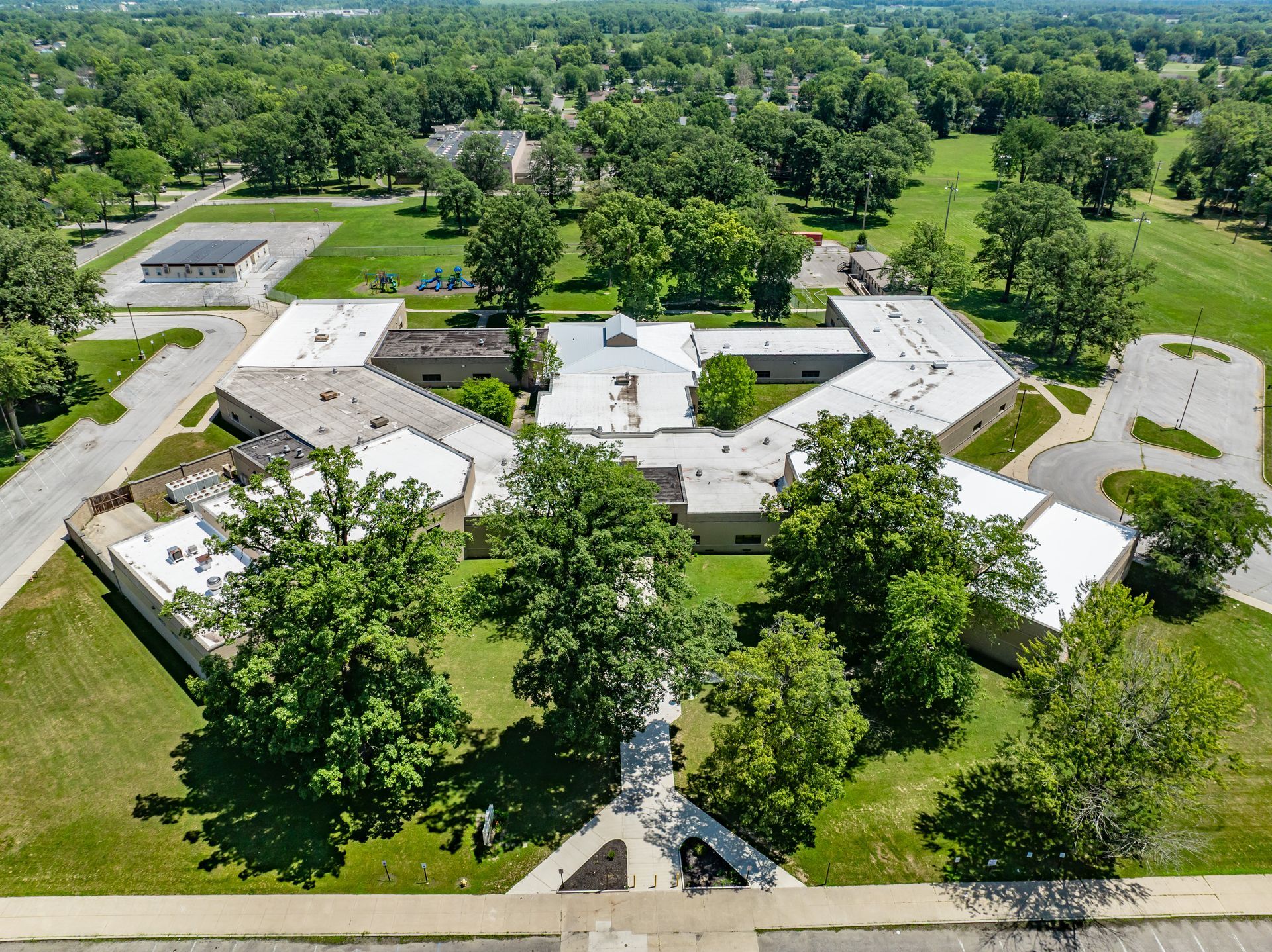 Aerial view of a white-roofed building complex surrounded by trees and parking lots on a green campus.
