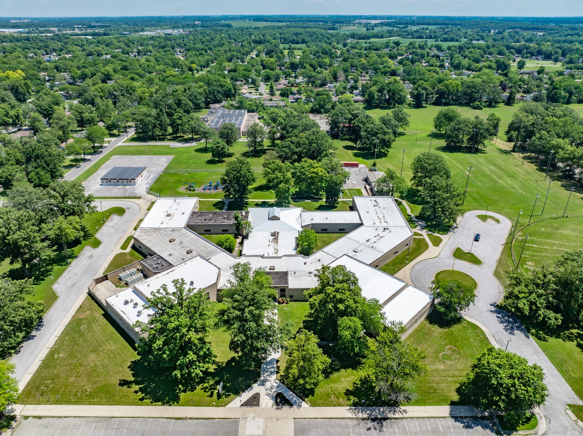 Aerial view of a white-roofed building complex surrounded by green trees and parking lots