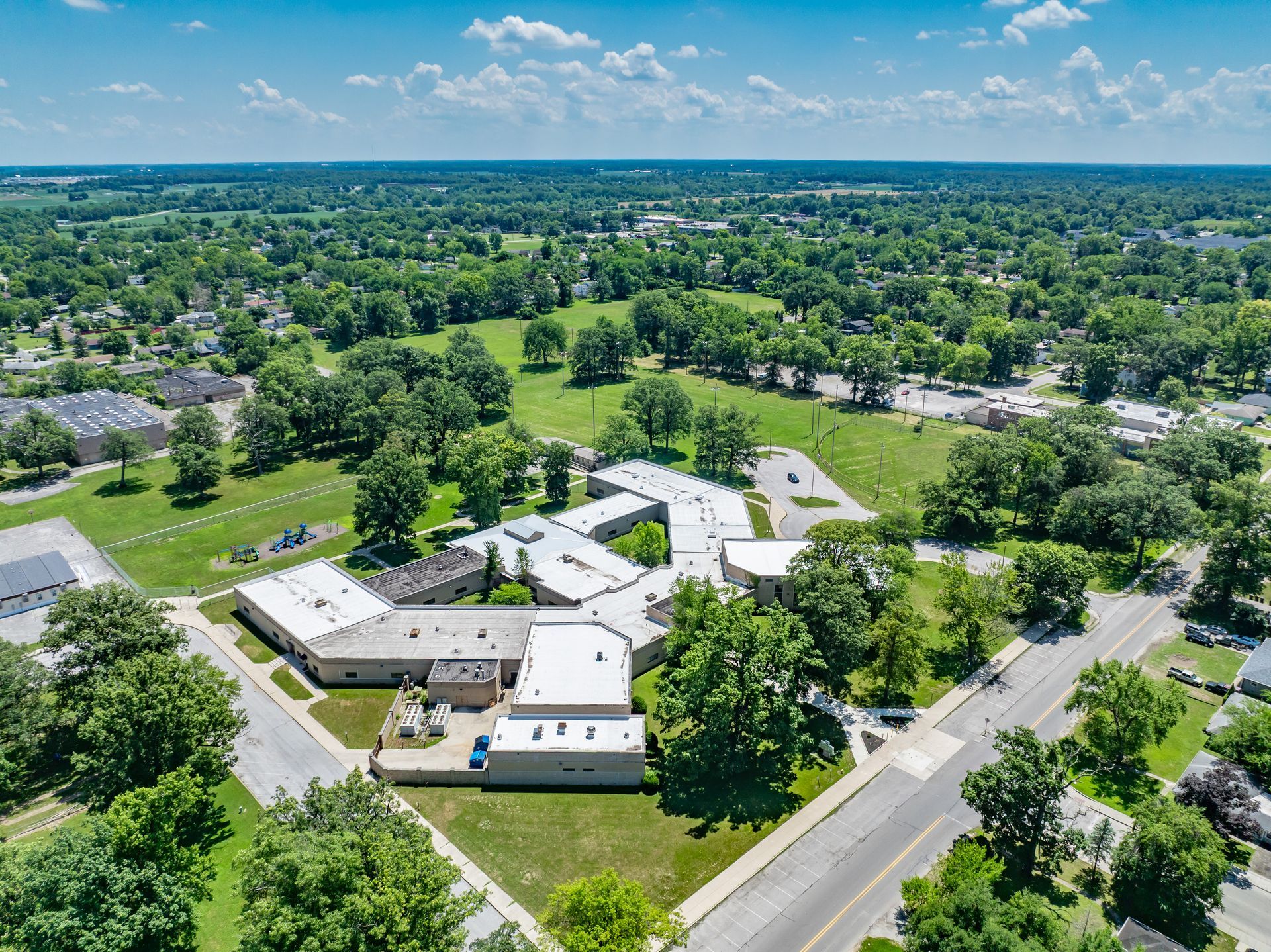 Aerial view of a white-roofed building complex surrounded by green trees in a suburban neighborhood