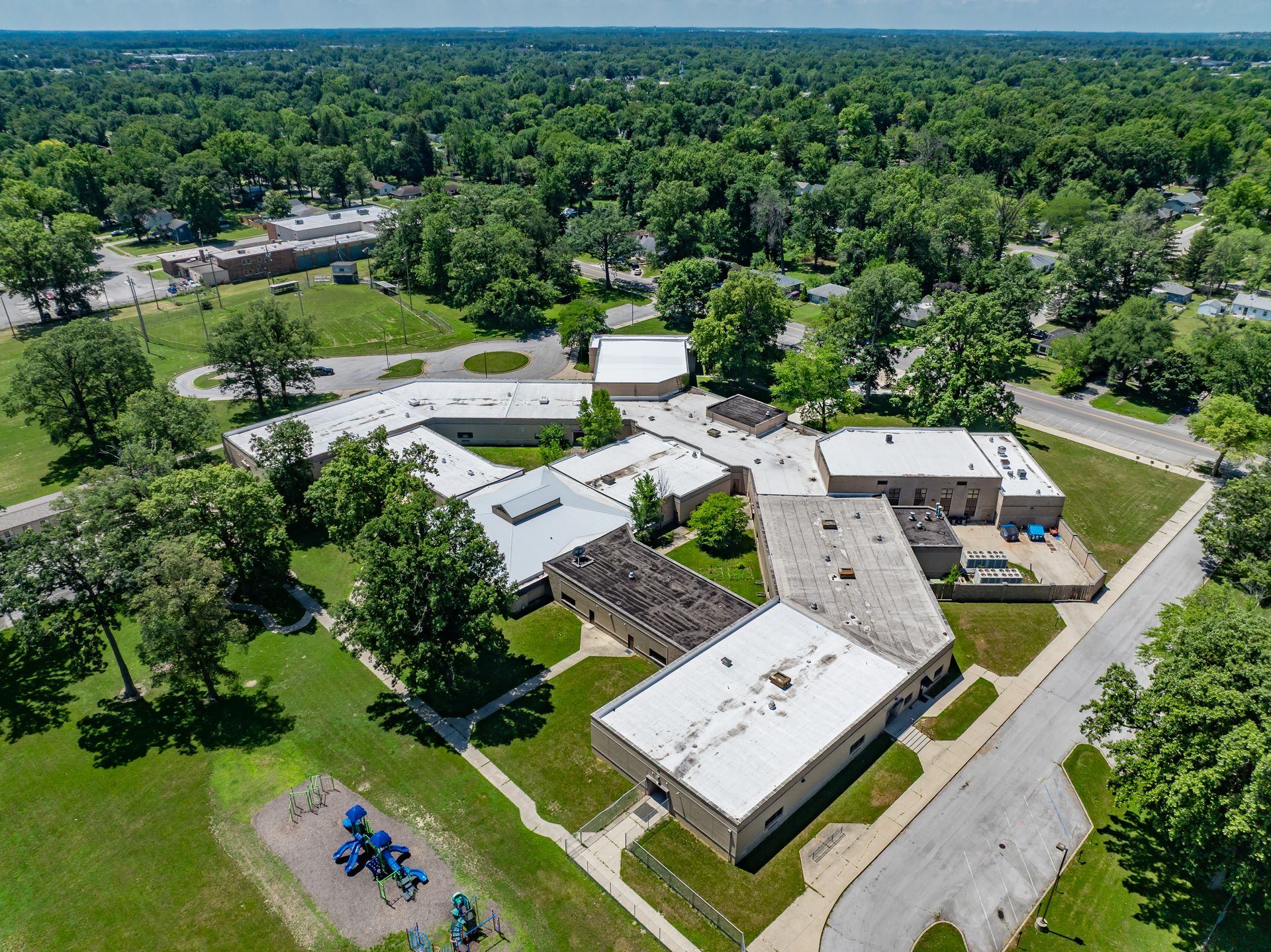 Aerial view of a small school campus surrounded by dense green trees and roads.