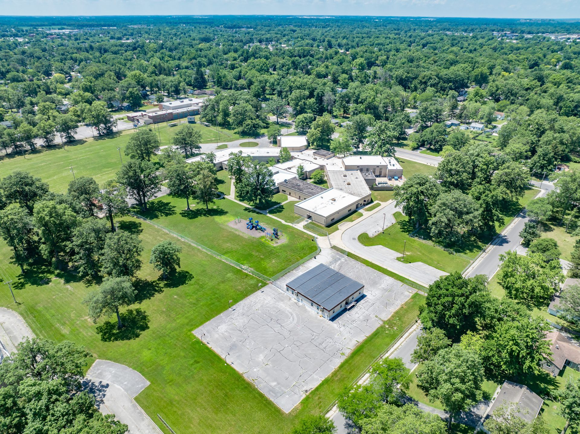 Aerial view of a rural campus with several white buildings, roads, and dense green trees.