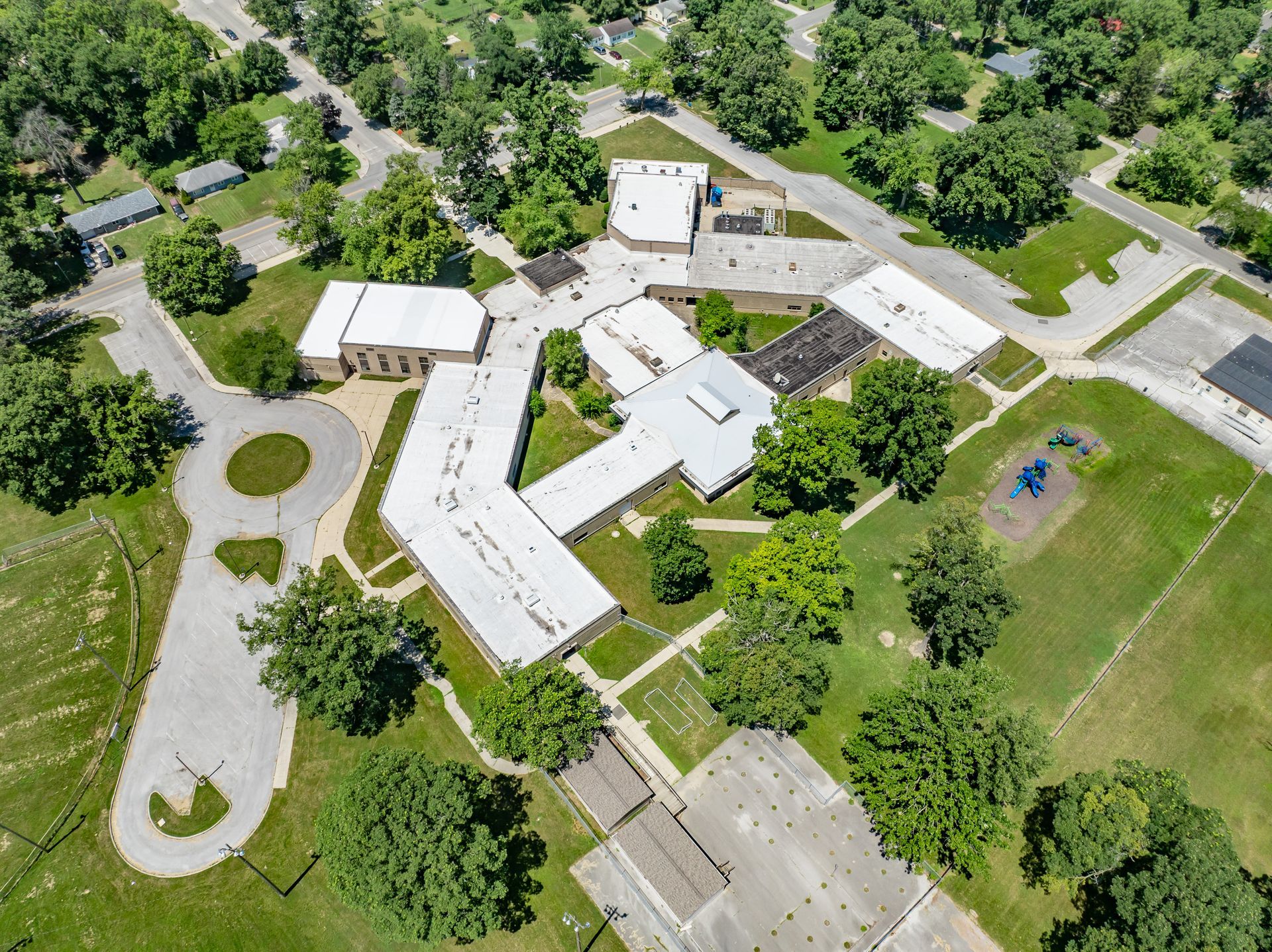 Aerial view of a school campus with white buildings, trees, walkways, and sports courts.