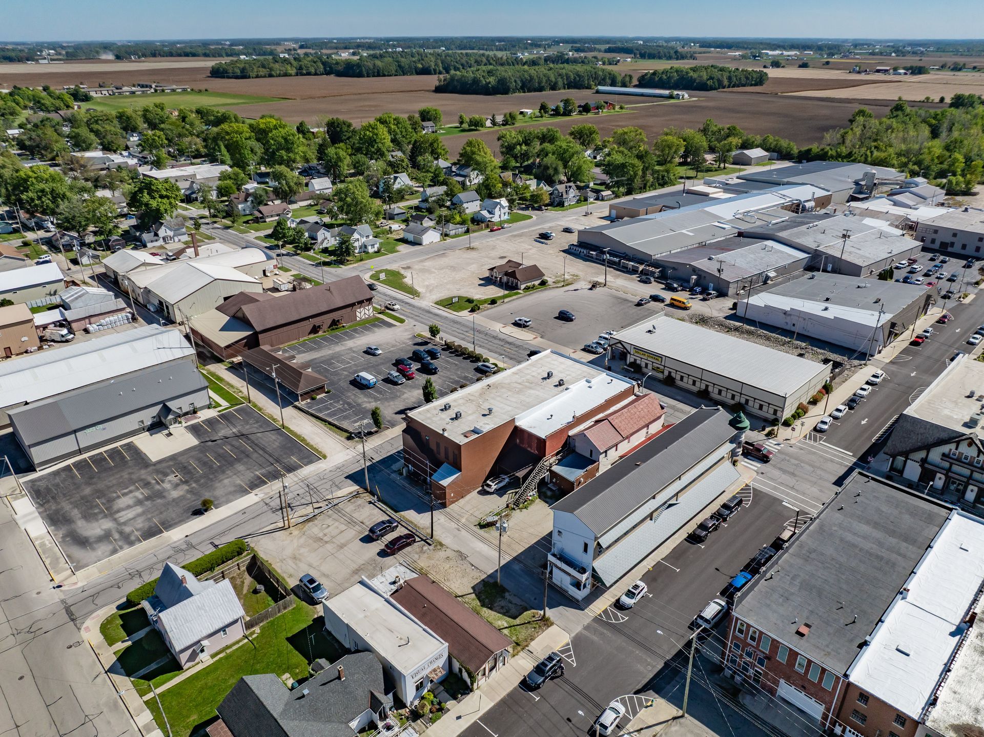 Aerial view of a small commercial district with parking lots, warehouses, and tree-lined streets