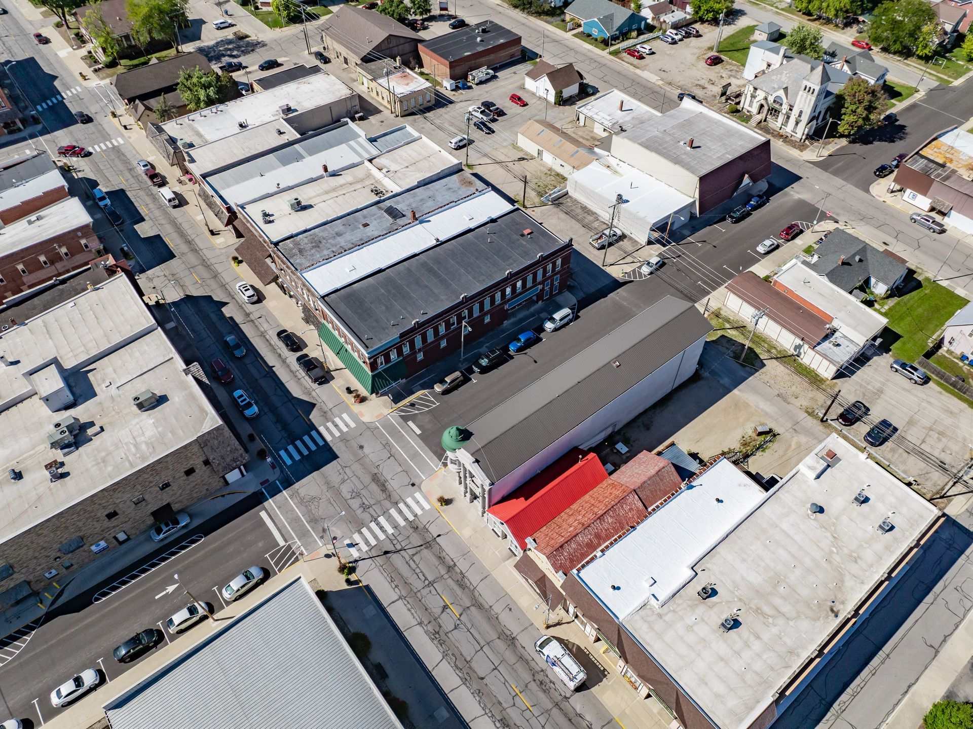 Aerial view of a downtown block with commercial buildings, streets, parked cars, and a crosswalk.
