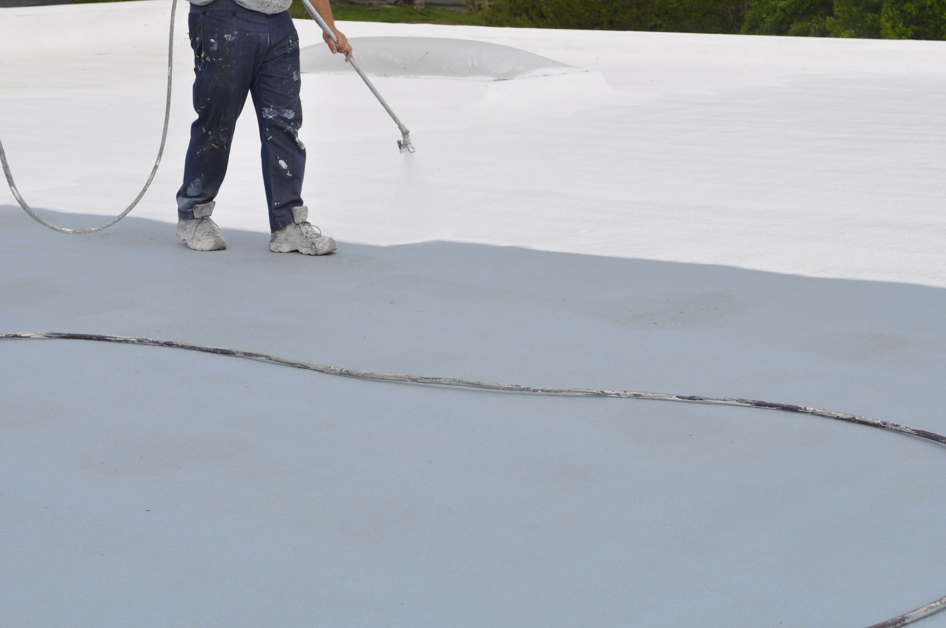 Worker spraying a white coating on a flat roof with a hose and wand