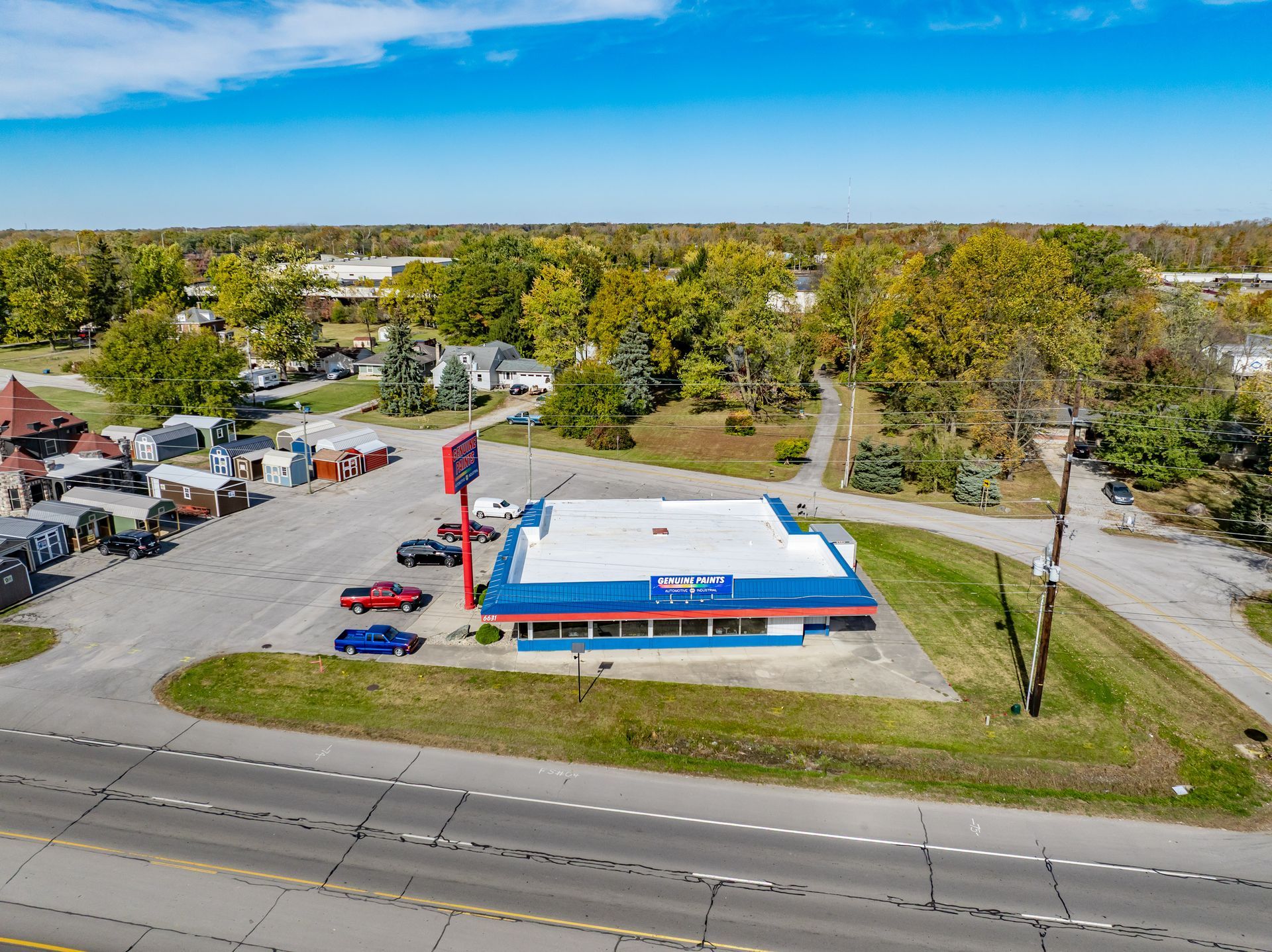 Aerial view of a roadside gas station with blue canopy, parked cars, and trees nearby.