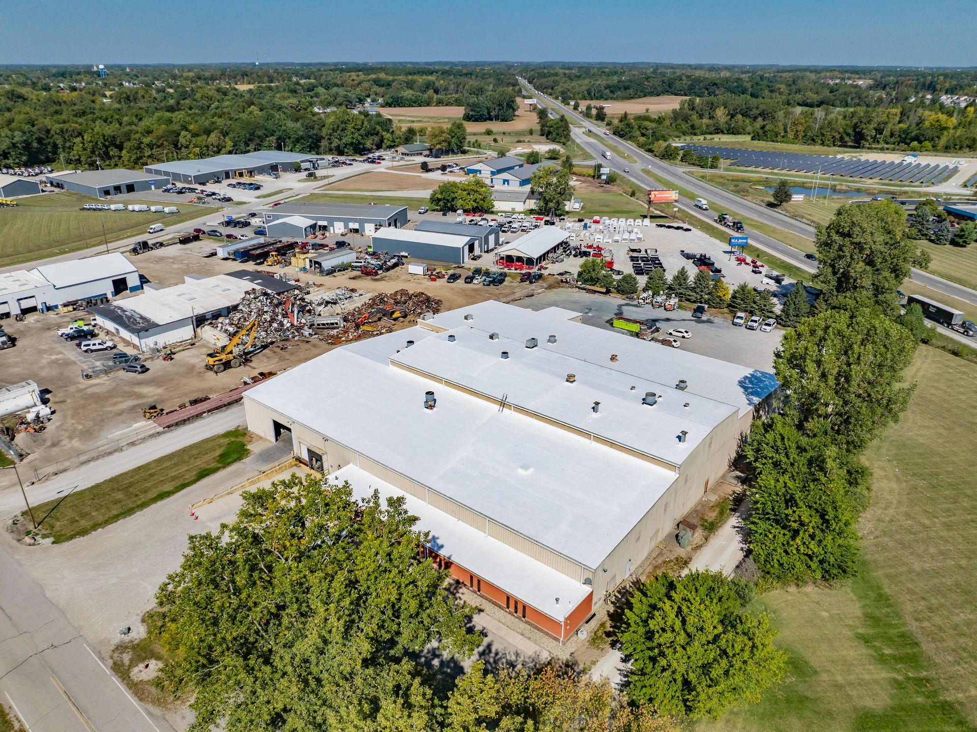 Aerial view of a large white-roofed industrial building with construction activity and surrounding roads.