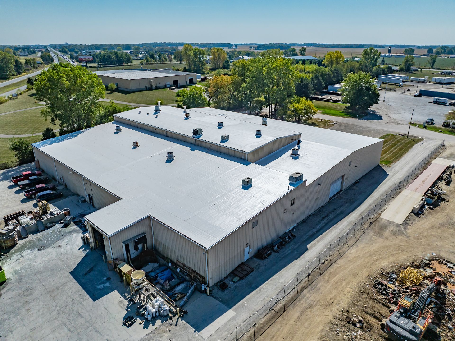 Aerial view of a large white industrial warehouse with rooftop vents and surrounding roads and lots.