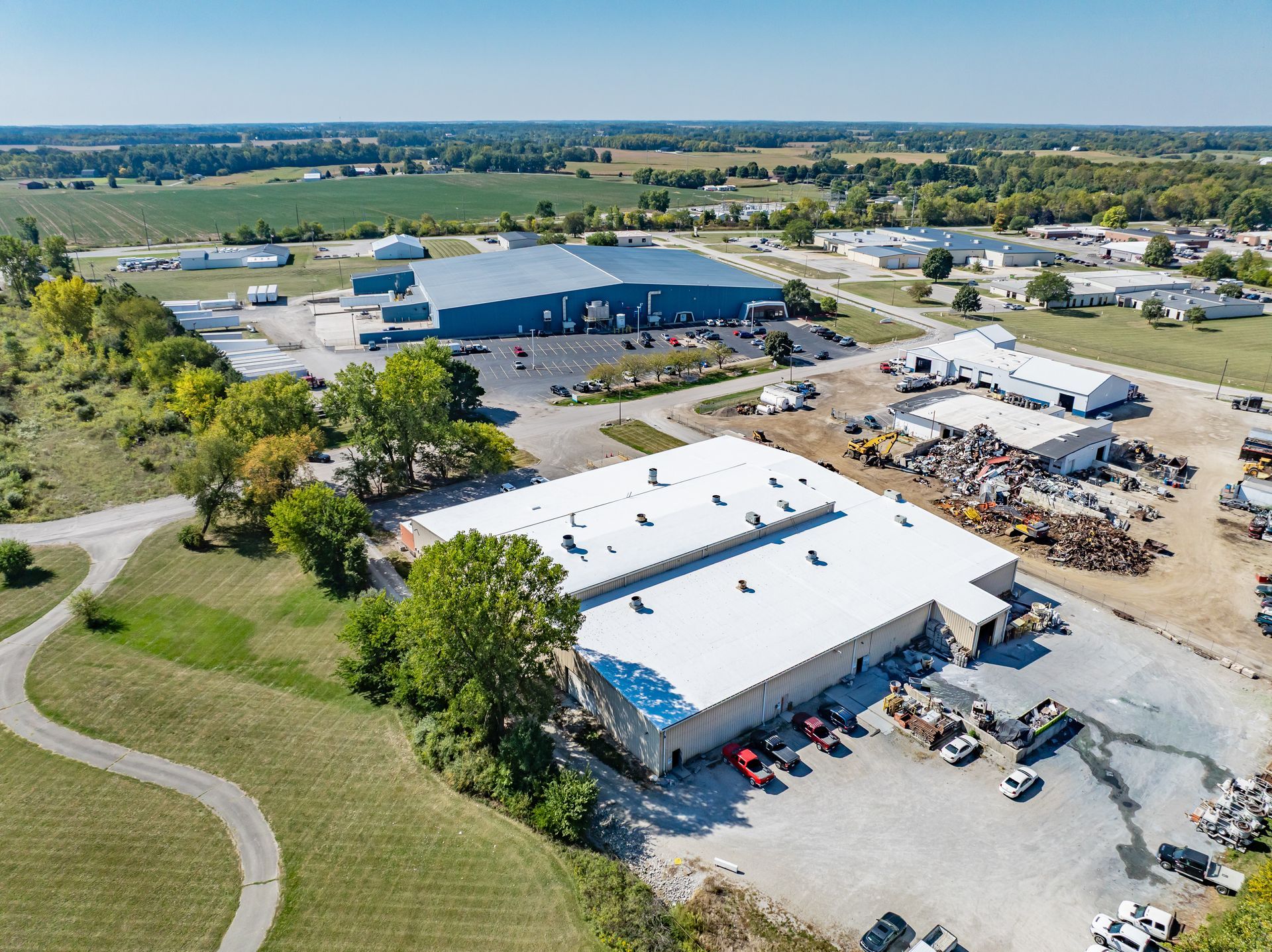 Aerial view of an industrial site with large white and blue warehouse buildings, trucks, and open lots.