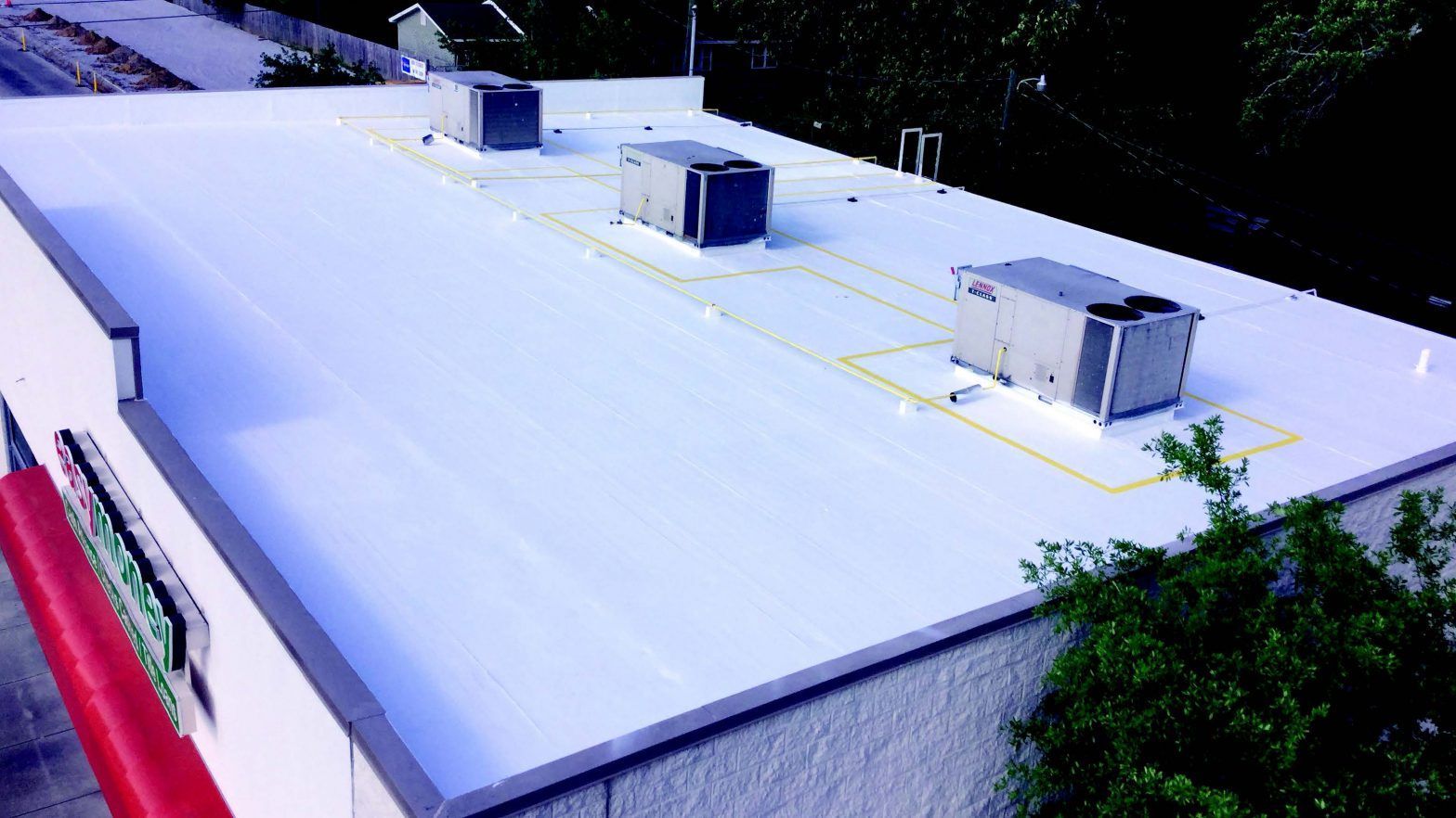 Flat white rooftop with two HVAC units and surrounding trees on a building.