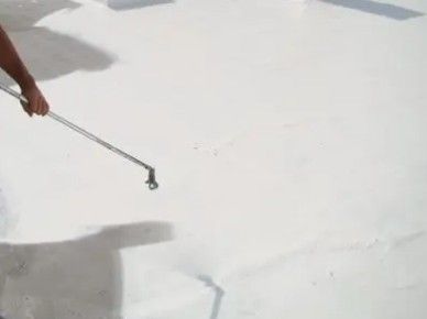 Person spraying white paint onto a floor with a long-handled roller