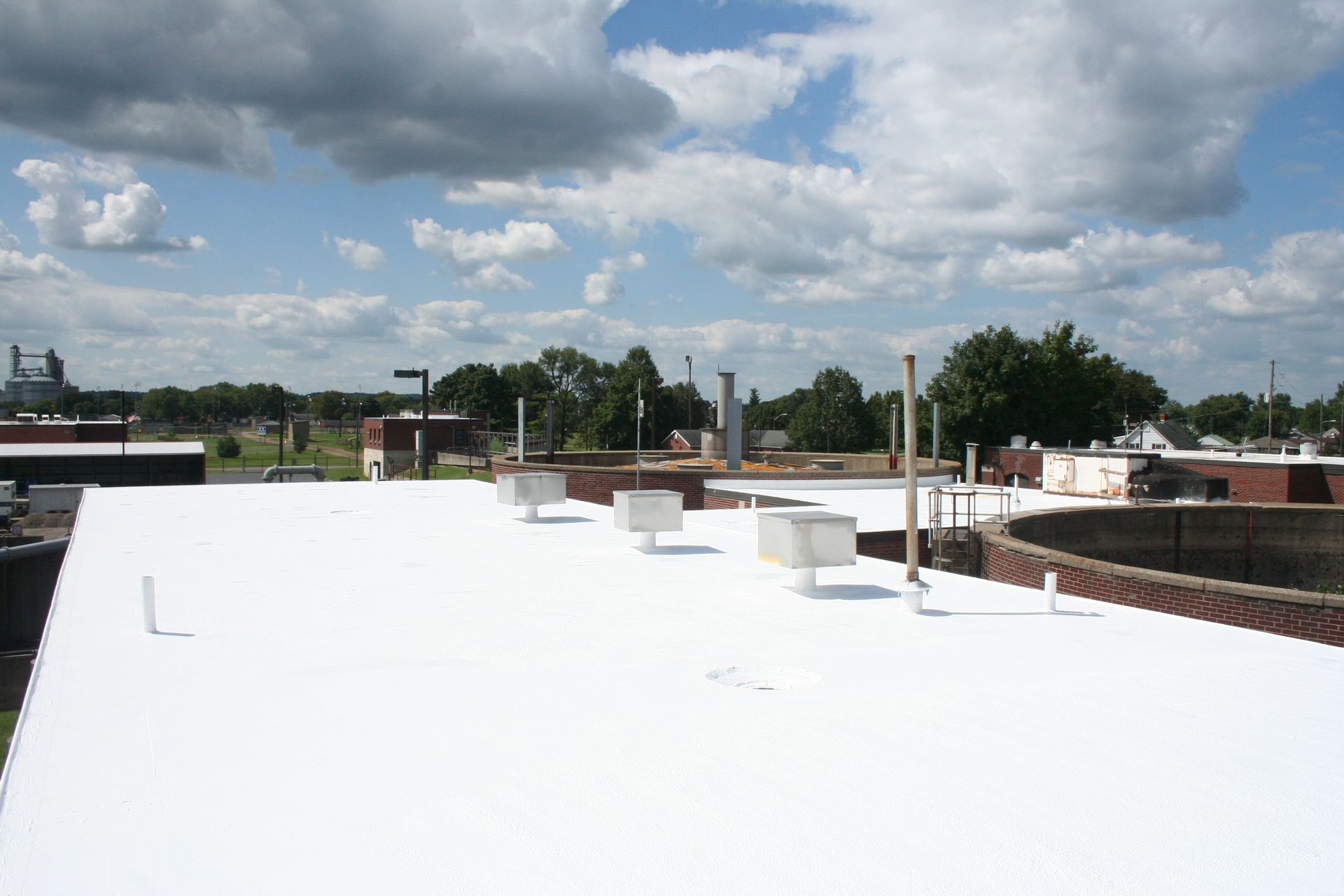 White flat rooftop with vents under a cloudy blue sky